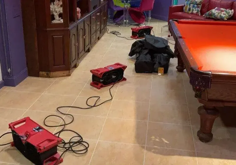 Red air movers drying the tile floor of a basement recreation room