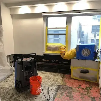 A dehumidifier and an air mover drying a room where the flooring has been pulled up and the floor is bare