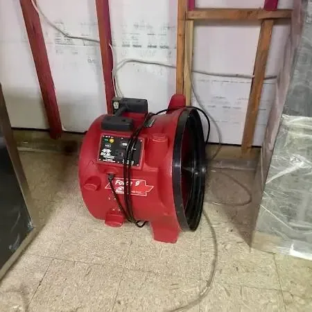 A red air mover drying a room with the lower wall opened and plastic sheeting hung to hold the work area