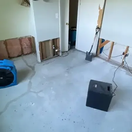 Air movers and a dehumidifier drying a room after the lower drywall was cut away and the floor left bare