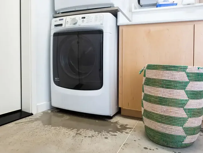 Water on the floor beside a washing machine after a leak