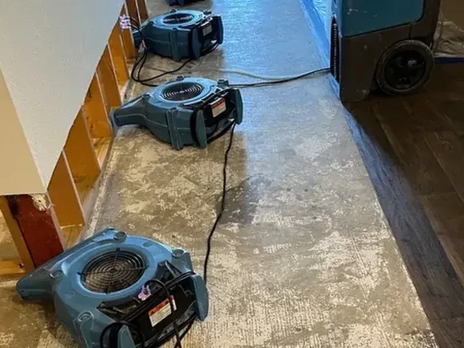An air mover and a dehumidifier drying a floor after a water loss