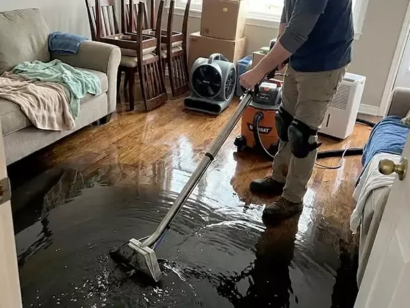 An extraction wand pulling standing water off a flooded hardwood floor in a living room